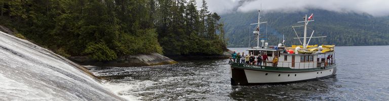 The Columbia III noses into a low angle waterfall in Tribune Channel for guests to take pictures while on a photo-tour in the Broughton Archipelago